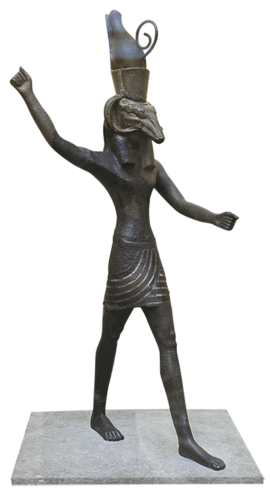 Escultura. Figura humana vestindo tecido ao redor da cintura e chapéu na cabeça. Tem nariz longo e pontiagudo. O braço direito está erguido para trás e, o braço esquerdo, esticado para baixo e para frente.