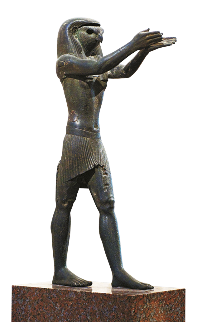 Escultura. Figura humana vestindo tecido ao redor da cintura e com cabeça de falcão. Ela está com as duas mãos erguidas para frente e com as palmas voltadas para cima.
