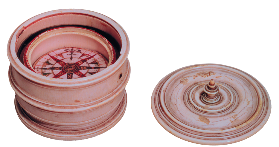 Fotografia. Bússola do século 16, em forma de um tubo. Dentro, há a representação da rosa dos ventos. Ao lado, uma tampa.