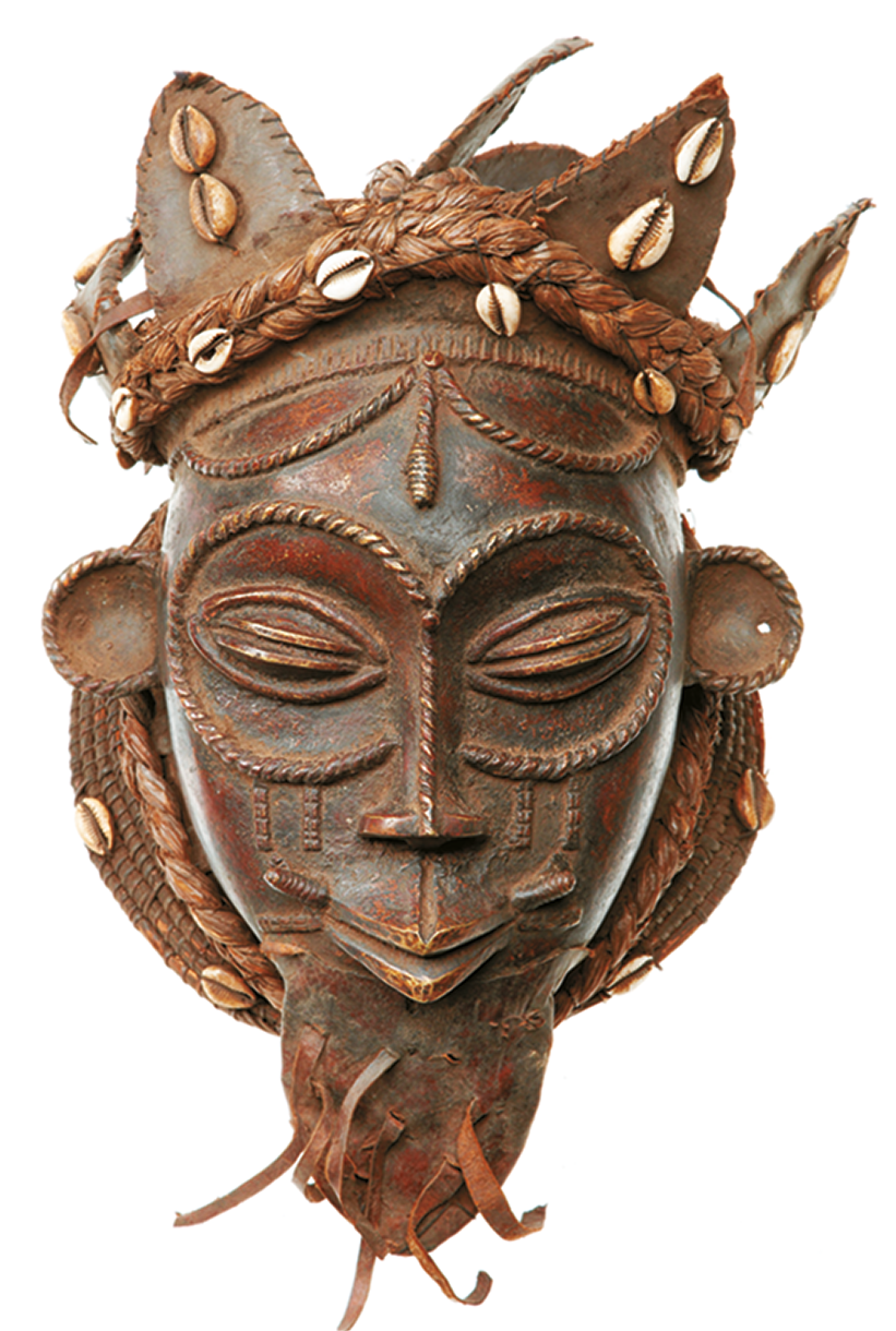 Fotografia. Máscara marrom com características da face de uma pessoa, destacando detalhes ao redor dos olhos e da testa e uma espécie de coroa decorada com conchas na cabeça.