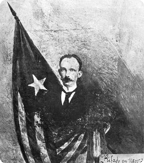 Fotografia em preto e branco. Um homem com bigode, usando terno, está com uma bandeira ao redor do corpo. A bandeira é composta por uma estrela dentro de um triângulo e listas.