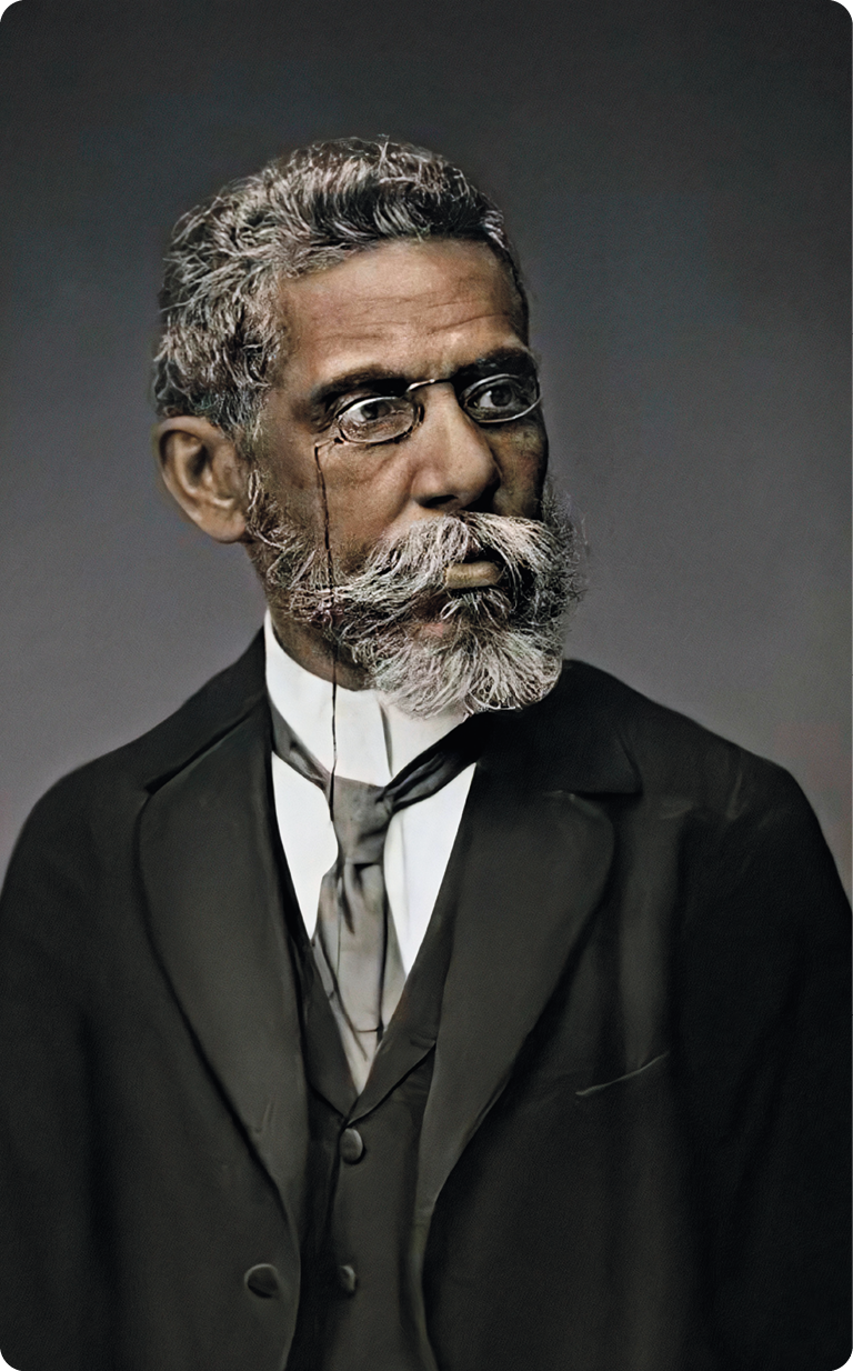 Fotografia. Destacando o busto de um homem negro, com cabelos e barba branca, usado óculos, gravata, colete e terno escuro.