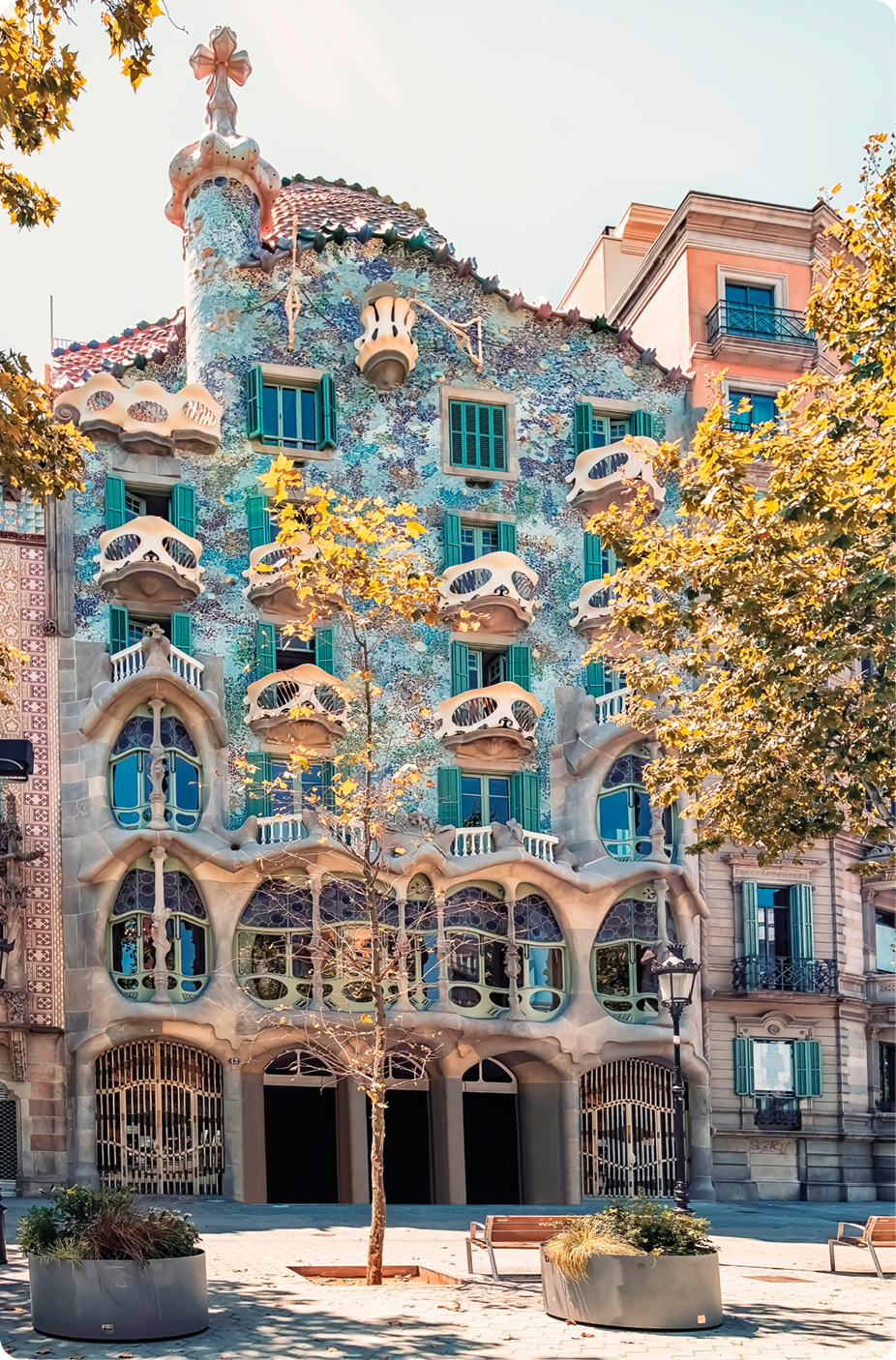 Fotografia. Fachada de edifício com cinco andares e muitas janelas, algumas com formato retangular e outras em formato circular. A fachada é azul com tons de verde e cor-de-rosa.