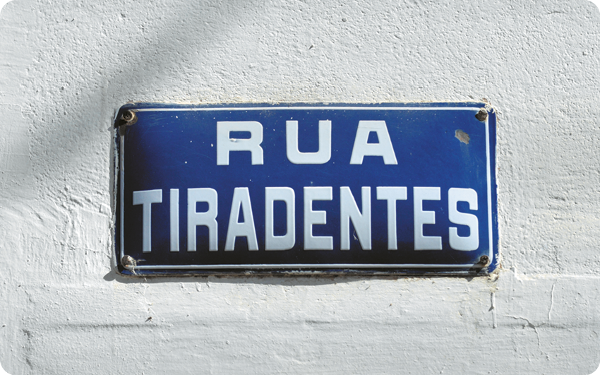 Fotografia. Placa azul com o texto: RUA TIRADENTES.