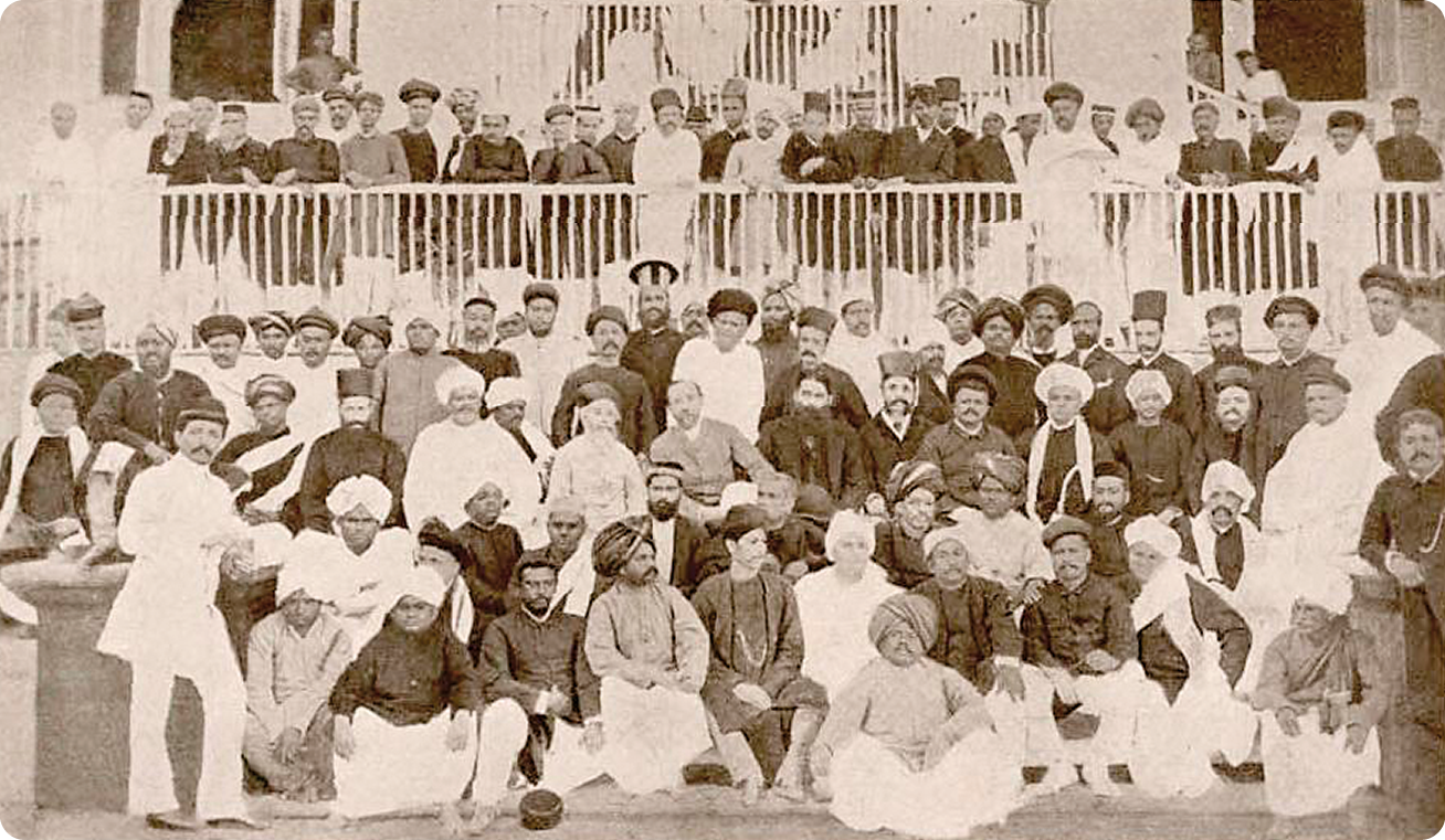 Fotografia. Diversos homens usando turbantes e túnicas. Alguns estão sentados e outros em pé.