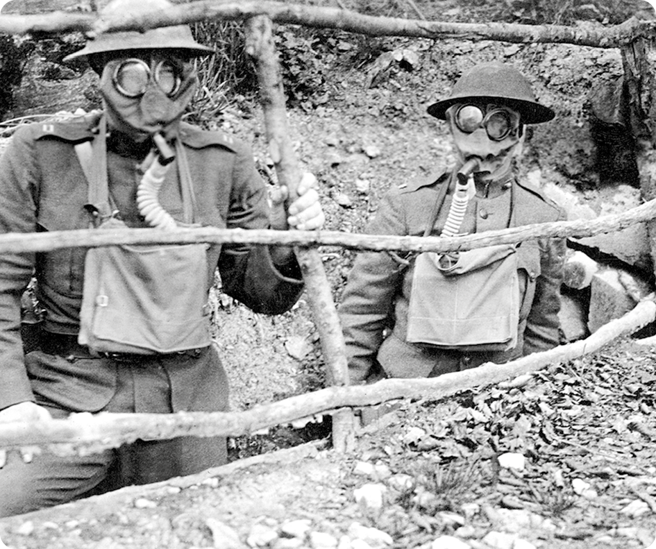 Fotografia em preto e branco. Dois soldados usando uma máscara cobrindo todo o rosto com um tubo respirador na parte inferior.