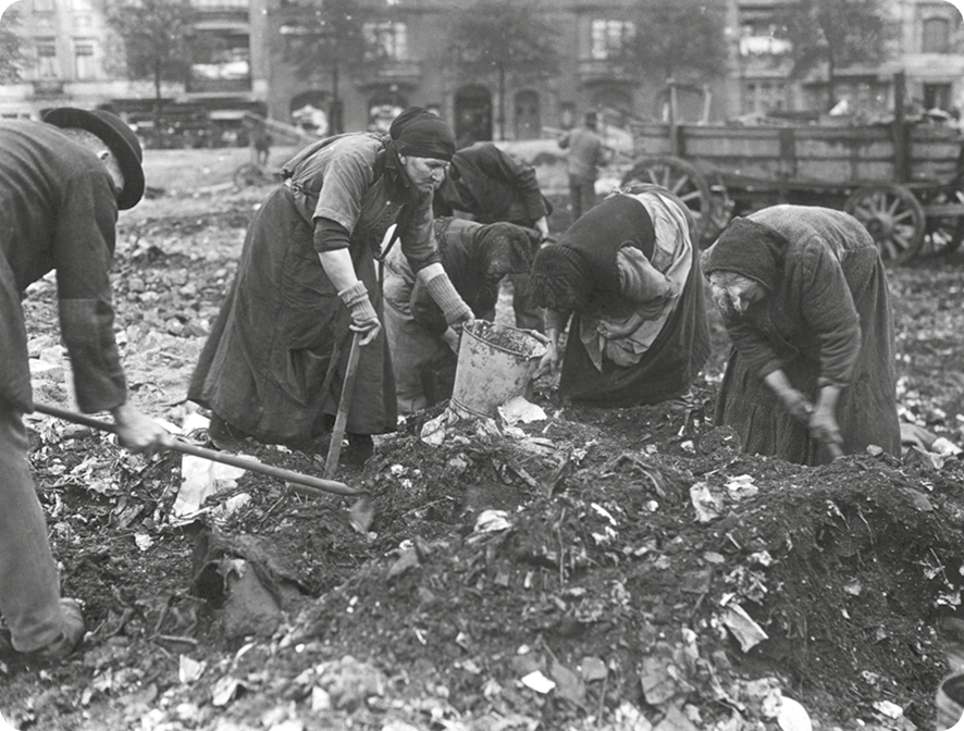 Fotografia em preto e branco. Mulheres usando vestidos e lenços na cabeças. Elas estão inclinadas sobre o lixo.