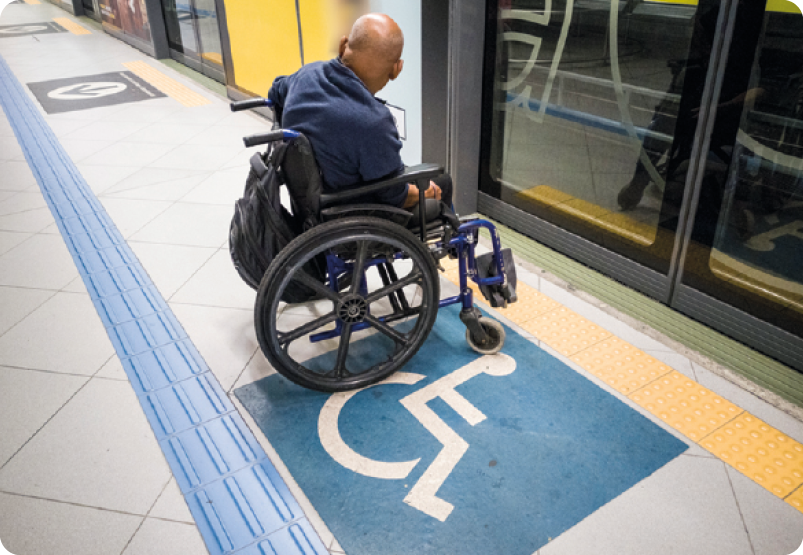 Fotografia. Um homem, usando blusa azul, está sentado em uma cadeira de rodas. Abaixo, um símbolo azul da silhueta de uma pessoa em uma cadeira de rodas.