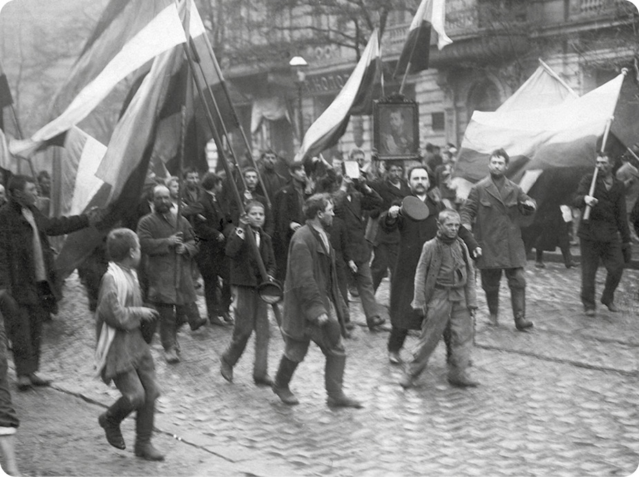 Fotografia em preto e branco. Pessoas caminhando em uma rua segurando bandeiras com as mãos.