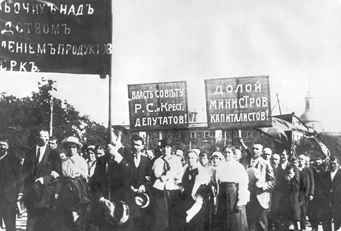 Fotografia em preto e branco. Homens e mulheres parados em uma rua segurando cartazes.