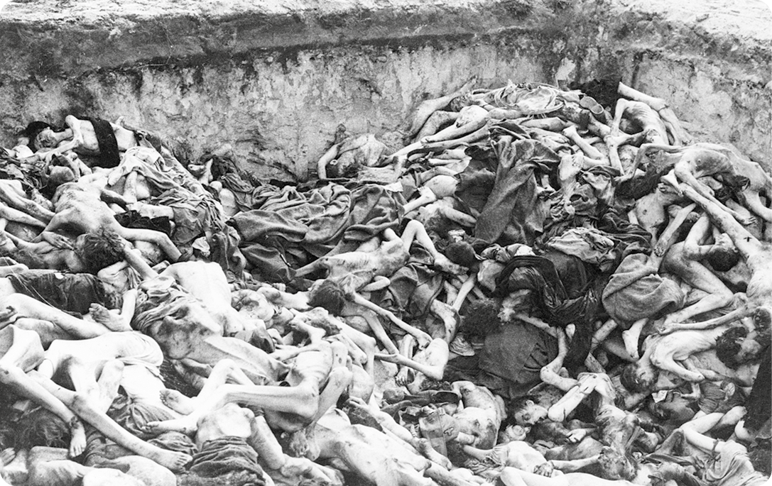 Fotografia em preto e branco. Vários corpos de pessoas, alguns estão sem vestes e sobrepostos dentro de uma vala.