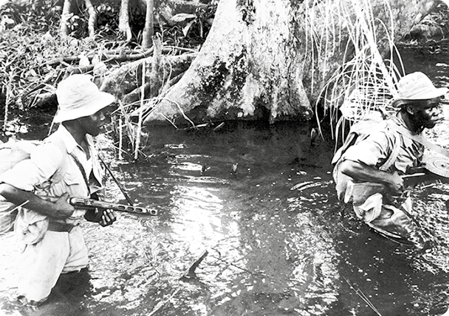 Fotografia em preto e branco. Dois homens negros, usando chapéu e blusa e com armas em punho, estão caminhando por um corpo de água que os encobre até a cintura. Atrás, árvores.