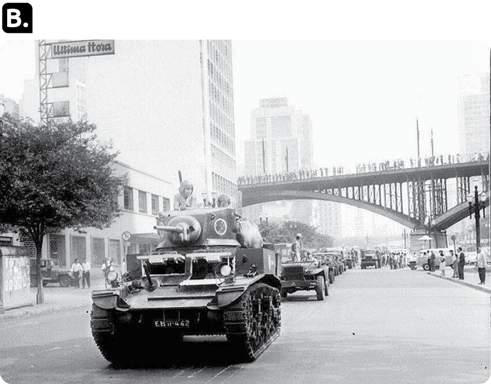 Fotografia em preto e branco 'B'. Uma fila de tanques de guerra em uma rua. Ao fundo, viaduto com várias pessoas e edifícios.