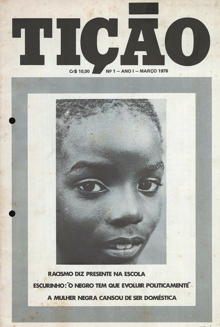 Capa de revista. Na parte superior, o nome da revista: TIÇÃO. Abaixo, fotografia destacando o rosto de uma criança negra. Na parte inferior, o texto: RACISMO DIZ PRESENTE NA ESCOLA. ESCURINHO: 'O NEGRO TEM QUE EVOLUIR POLITICAMENTE'. A MULHER NEGRA CANSOU DE SER DOMÉSTICA.