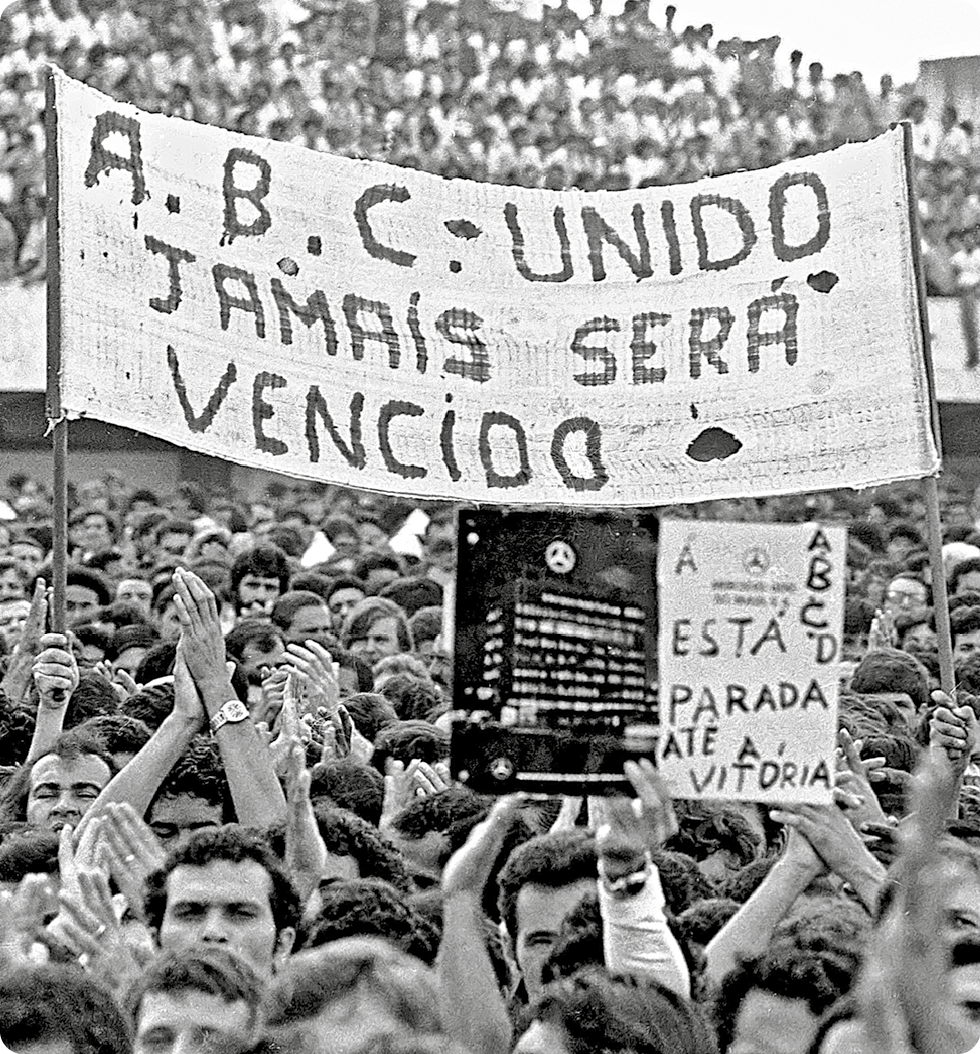 Fotografia em preto e branco. Diversas pessoas segurando um cartaz com o texto: A. B. C – UNIDO JAMAIS SERÁ VENCIDO.