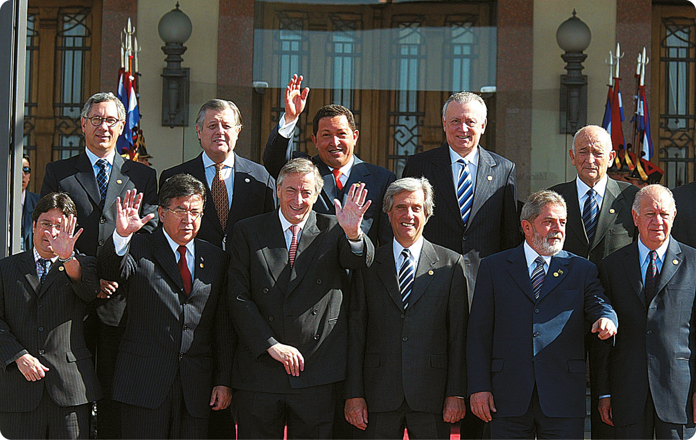 Fotografia. Vários Homens usando terno. Eles estão de pé com as mãos levantadas.