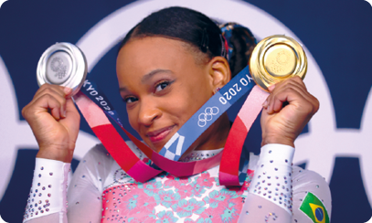 Fotografia da atleta Rebeca Andrade. A garota segura, sorridente, duas medalhas: uma de ouro e outra de prata.