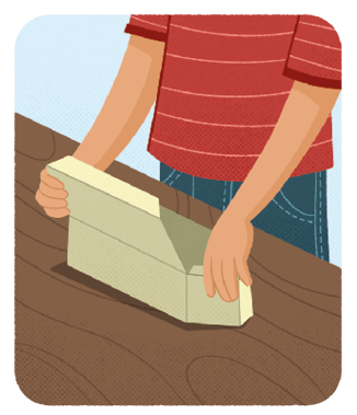 Ilustração das mãos de um menino desmontando uma caixa de papel, de formato de um paralelepípedo reto retângulo, que está em cima de uma mesa. Nesse momento o menino está abrindo as faces laterais da caixa e a face de cima.