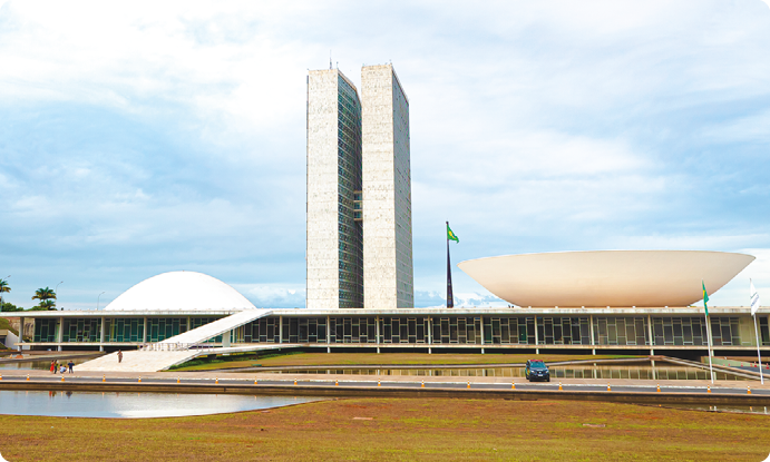 Fotografia de um  edifício horizontal, com uma rampa central, duas torres de edificação no centro e uma semi esfera a cada lado, acima do bloco horizontal, uma voltada para cima e outra para baixo.