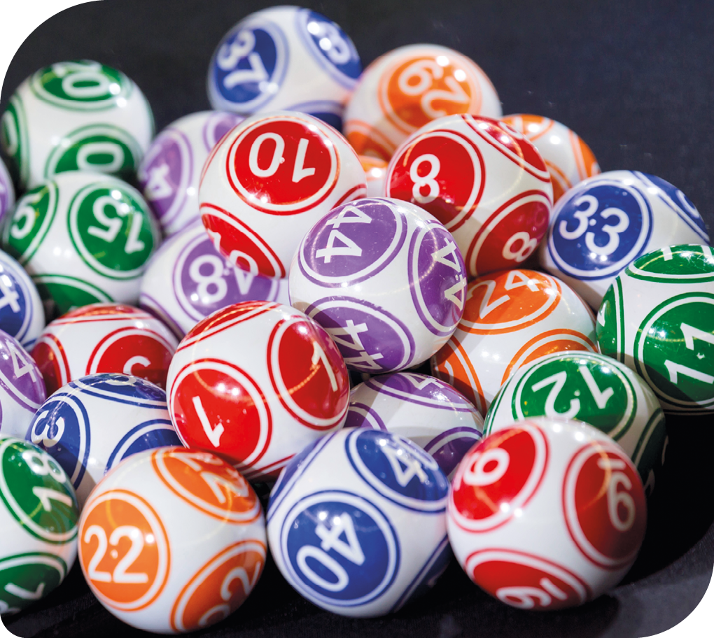 Fotografia. Há várias bolas utilizadas em sorteios de jogos e loterias. As bolas são coloridas e todas apresentam números. Elas estão umas sobre as outras.