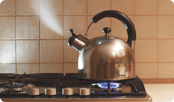 Fotografia de uma chaleira saindo vapor, em cima de um fogão acesso.