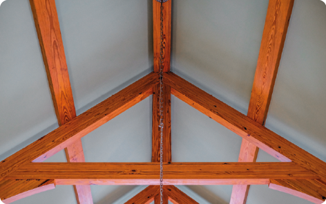 Fotografia da vista de baixo de um telhado, com sua estrutura de madeira possuindo formato triangular.