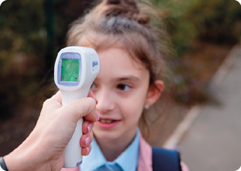 Fotografia da mão de alguém medindo a temperatura corporal de uma menina com um termômetro infravermelho.