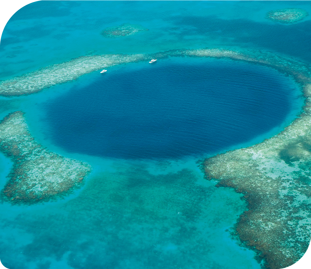 Fotografia do mar, visto de cima, com uma parte mais azul em formato de círculo formada, com recifes de corais em volta.