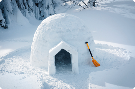 Fotografia da parte frontal de um iglu, em ambiente ártico, com neve aos arredores.