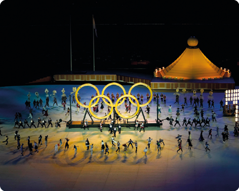 Fotografia de várias pessoas se apresentando em volta do símbolo das olimpíadas.