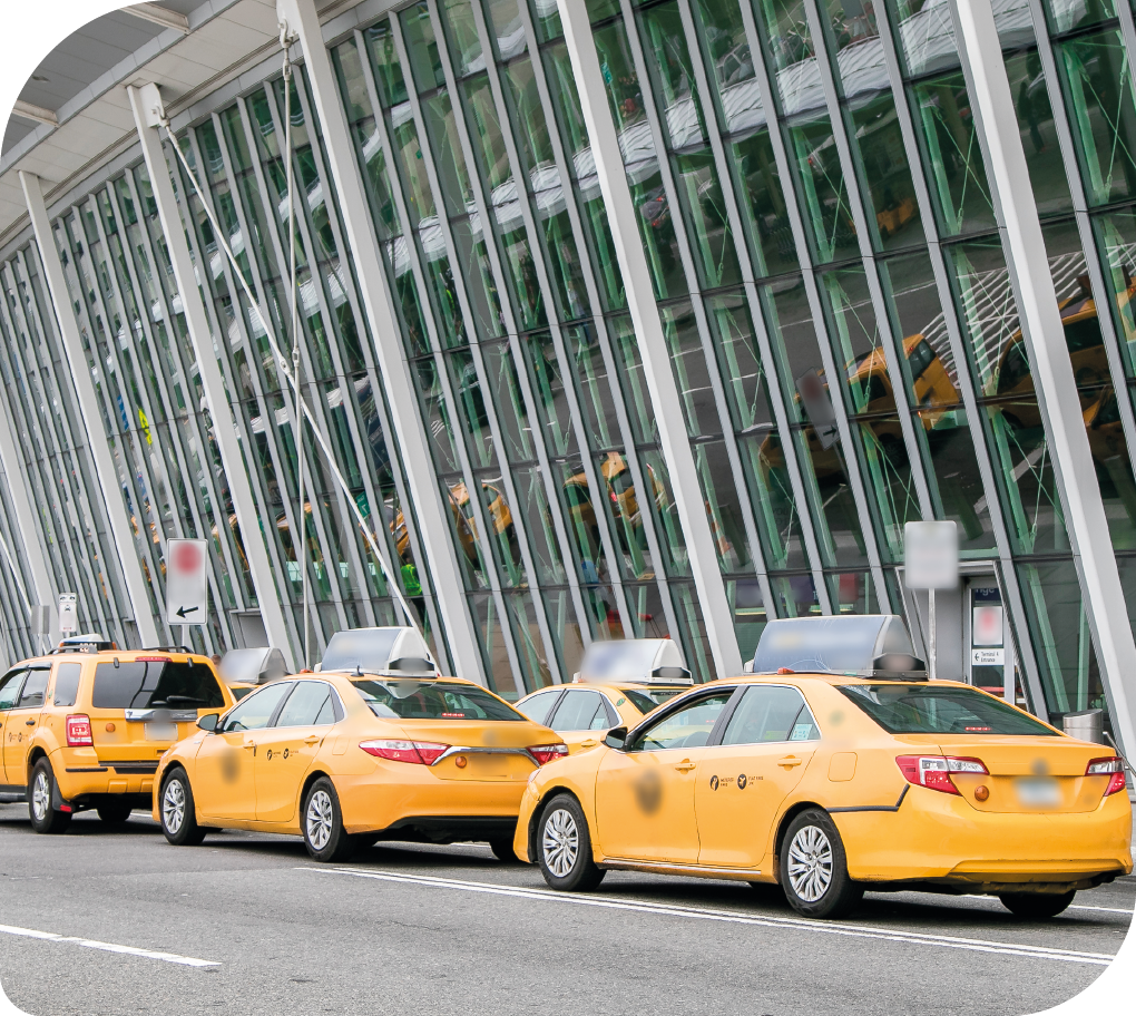 Fotografia de 3 carros táxis estacionados em frente à uma edificação.