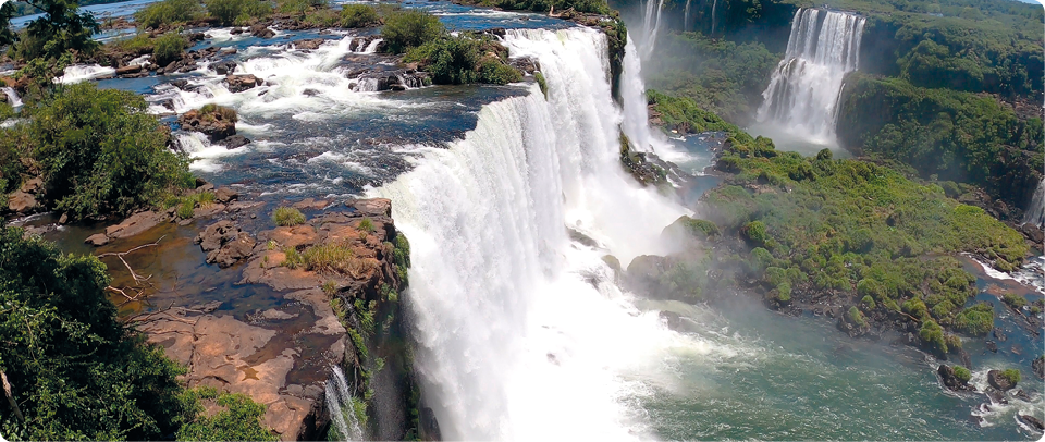 Fotografia com a vista superior de parte das Cataratas do Iguaçu. Nela estão as cataratas e a mata nativa da região.