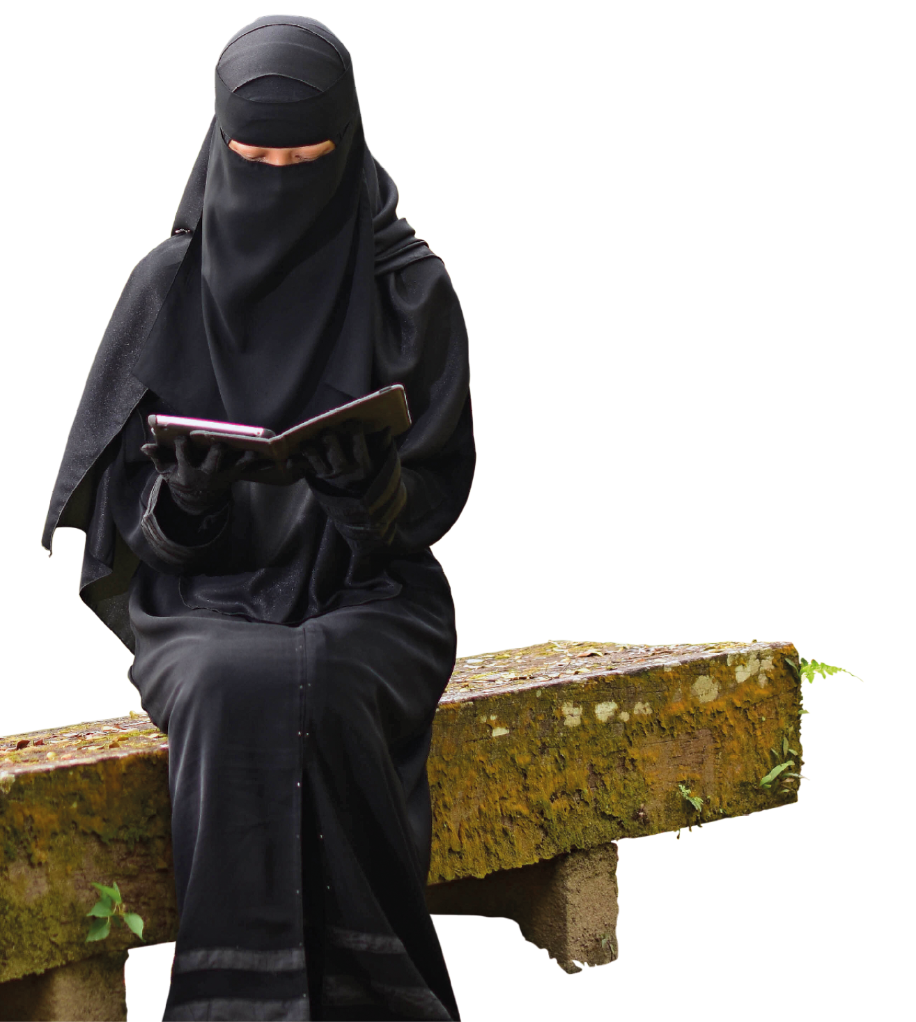 Fotografia. Uma mulher sentada sobre um banco de cimento de cor marrom. Ela usa roupa de cor preta que cobre todo seu corpo, inclusive a cabeça. Ela usa par de luvas da mesma cor. A mulher olha para baixo e segura nas mãos um livro de capa preta.