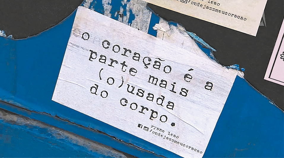 Lambe-lambe. Fundo de cor azul e partes em preto e bege. Ao centro, folha branca com texto datilografado em preto: o coração é a parte mais (o)usada do corpo.