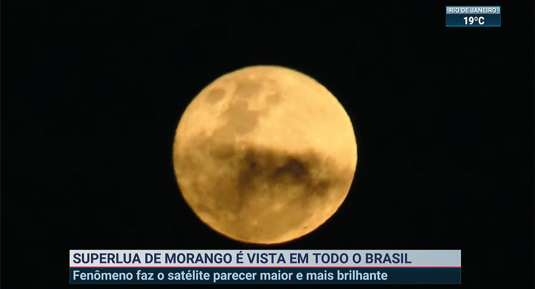 Captura de tela. Vista de céu noturno em preto e, ao centro, lua redonda em bege. Na parte inferior, texto: SUPERLUA DE MORANGO É VISTA EM TODO O BRASIL – FENÔMENO FAZ SATÉLITE PARECER MAIOR E MAIS BRILHANTE.