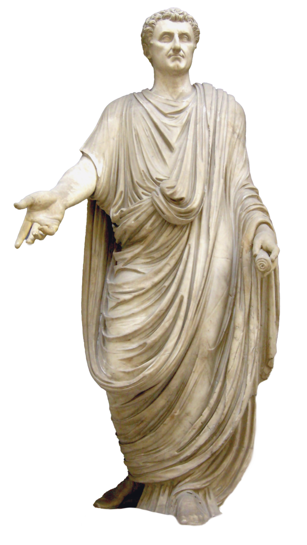 Fotografia. Estátua de um homem de cabelos curtos usando uma túnica longa com panos por cima, com os braços ligeiramente abertos, erguendo a palma de uma mão para frente.