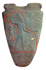 Fotografia. Parte frontal da Paleta de Narmer, com linha vermelha destacando uma cena. A cena em destaque representa um homem grande em pé, usando uma coroa comprida e afunilada de ponta arredondada, com uma das mãos levantadas segurando um bastão e a outra segurando a cabeça de um homem menor ajoelhado no chão.