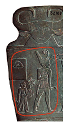 Fotografia. Detalhe do verso da Paleta de Narmer, com linha vermelha destacando uma cena. A cena em destaque mostra um homem grande usando uma coroa de base quadrada, com uma longa ponta atrás, e um fio enrolado saindo do meio. Ele segura um cetro. Atrás dele, à esquerda, um homem pequeno segurando um objeto.