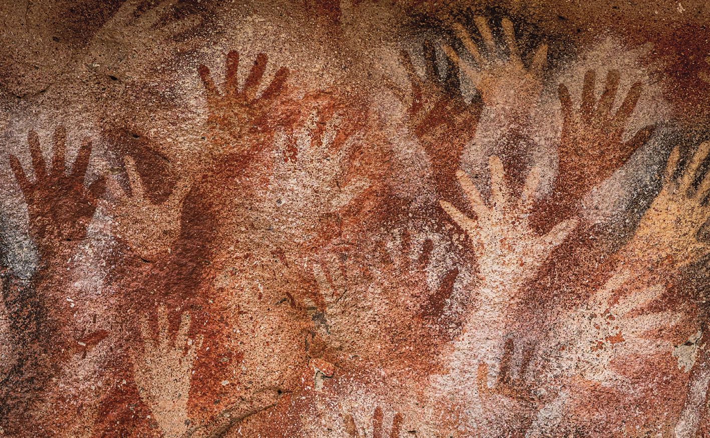 Fotografia. Várias palmas de mãos impressas na parede de uma caverna.