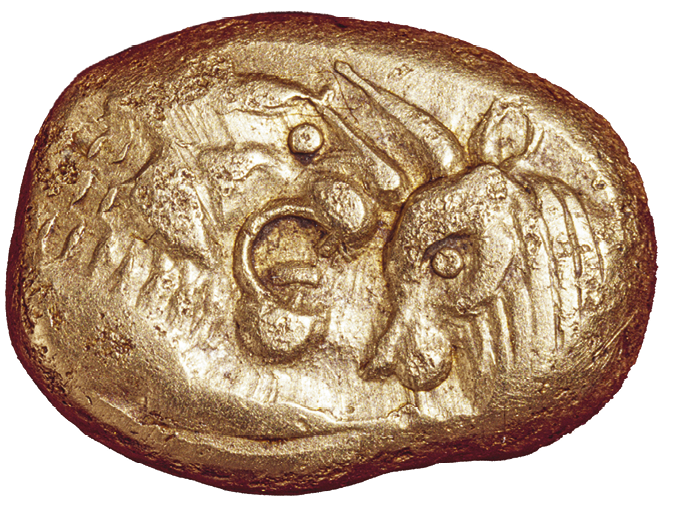 Fotografia. Artefato oval de ouro com desenhos da cabeça de um felino de frente para a cabeça de um animal com dois chifres.
