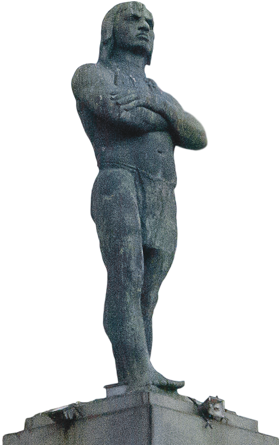 Fotografia. Estátua de um homem indígena em pé, de braços cruzados e vestindo uma tanga.
