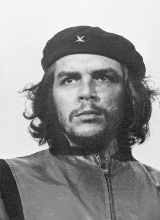 Fotografia em preto e branco. Ernesto Che Guevara, homem de olhos grandes, sobrancelhas cheias, rosto largo e boca pequena. Tem bigode e cavanhaque. O cabelo é comprido na altura das orelhas. Usa uma boina com uma estrela no centro. Olha para o horizonte.