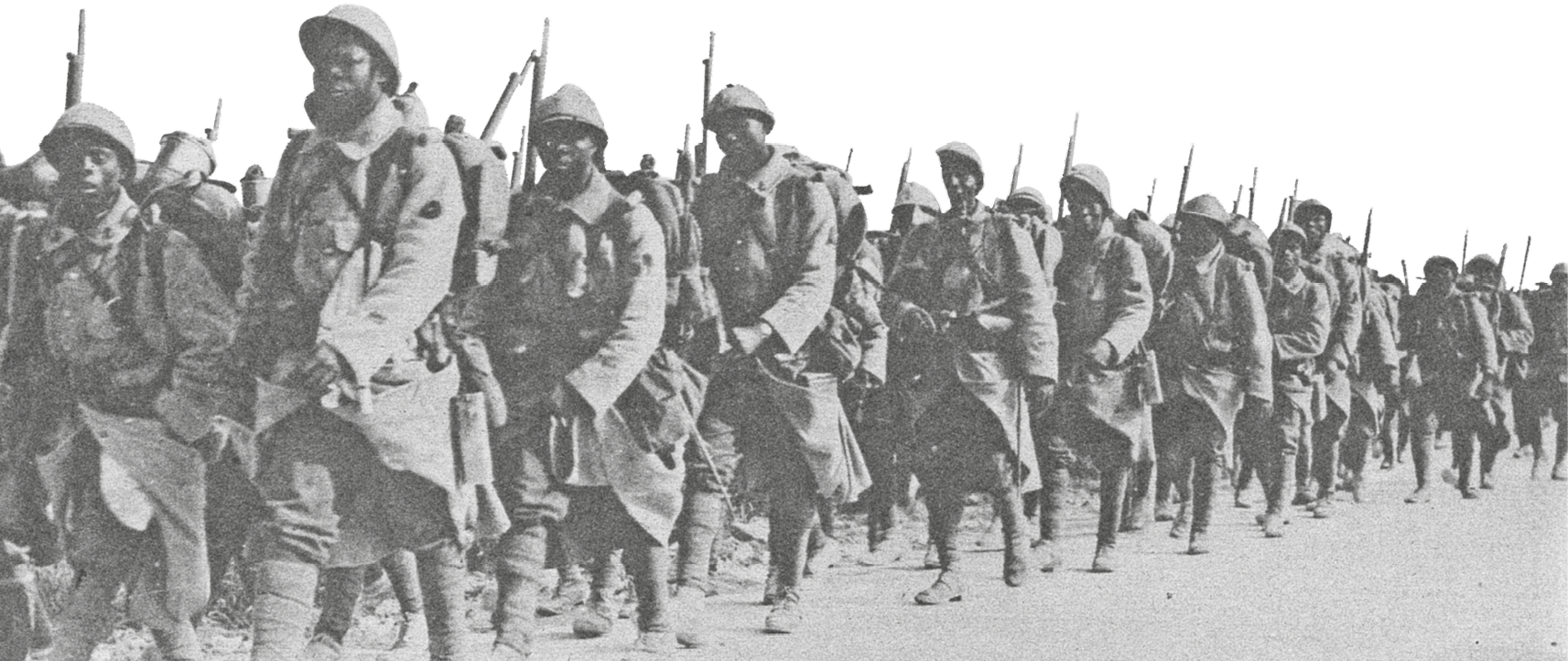 Fotografia em preto e branco. Soldados de uniforme, capacete e armas sobre o ombro. Estão marchando em filas.