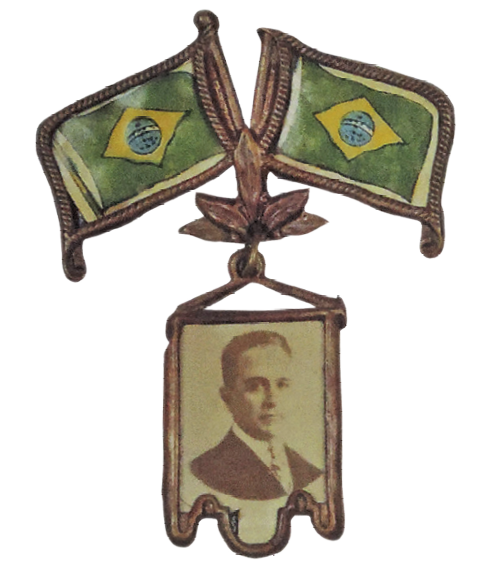 Fotografia. Broche com retrato de Getúlio Vargas encimado por duas bandeiras do Brasil.