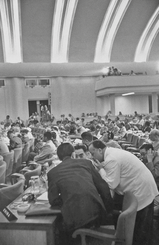 Fotografia em preto e branco. Homens reunidos em um grande salão. Estão em cadeiras dispostas em longas fileiras.