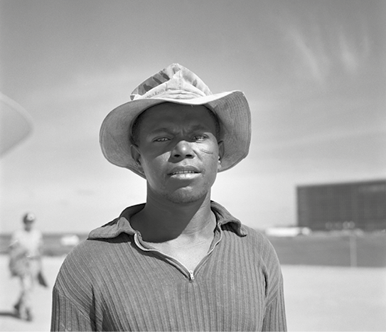 Fotografia em preto e branco. Homem de camisa e chapéu visto da cintura para cima.